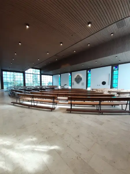 Moderner Innenraum der Kirche in Bad Zwischenahn mit Holzbänken und farbigen Glasfenstern