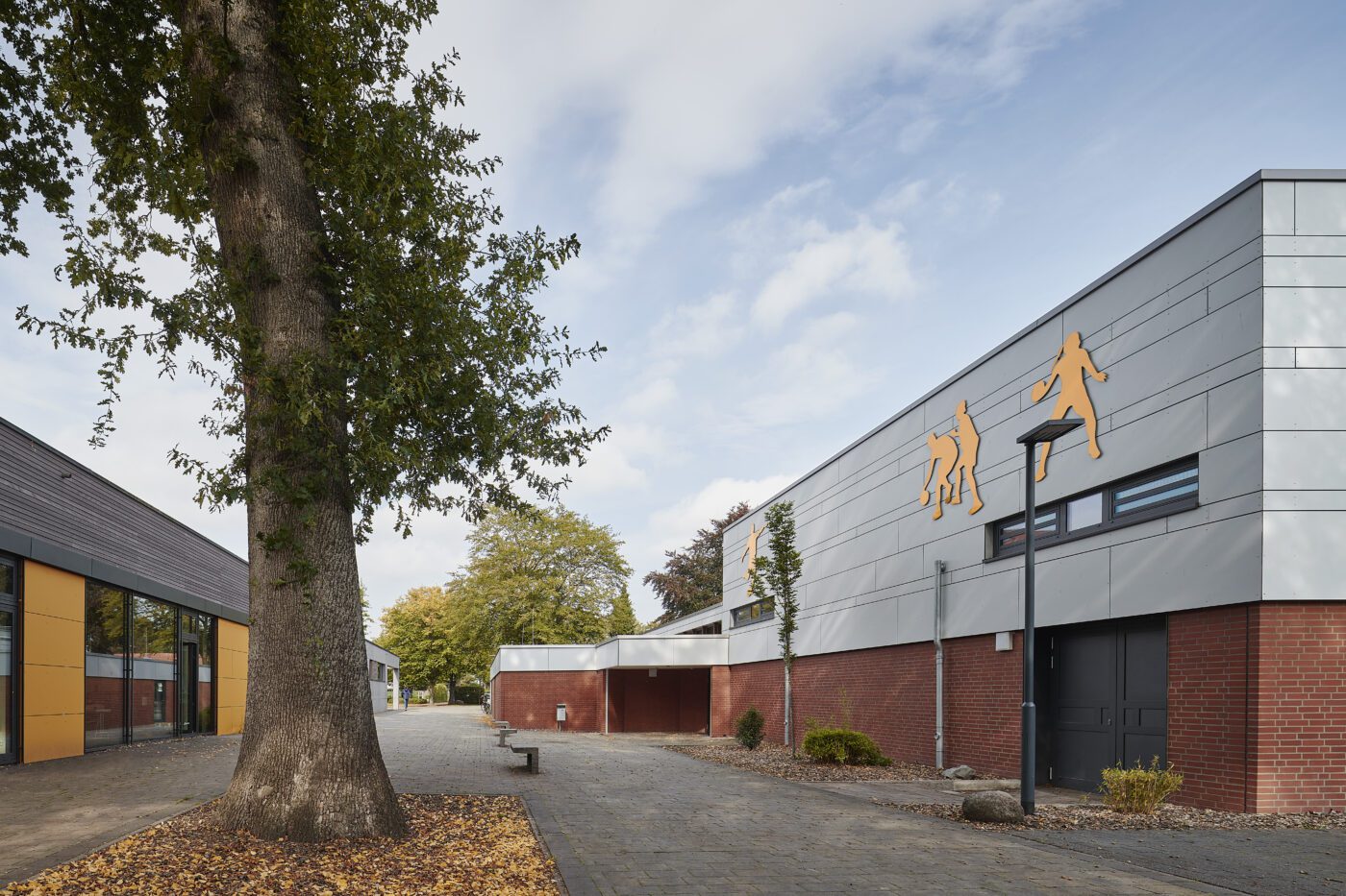 Moderner Schulhof mit Backsteingebäuden, Baum und Sportwanddekoration unter blauem Himmel