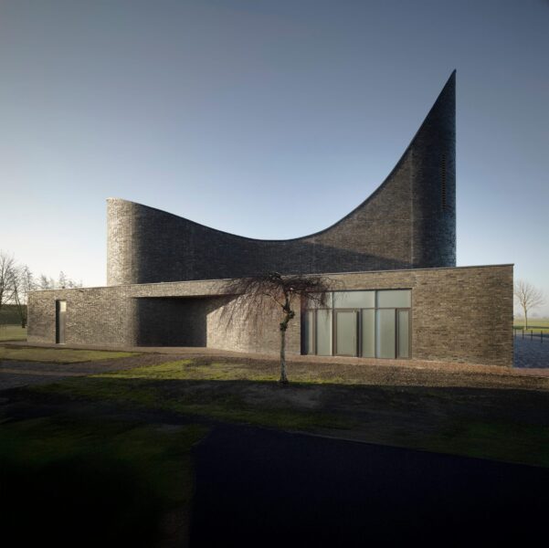 Moderne Kirche mit geschwungener Ziegeldachkonstruktion im Tageslicht, umgeben von Gras und Bäumen