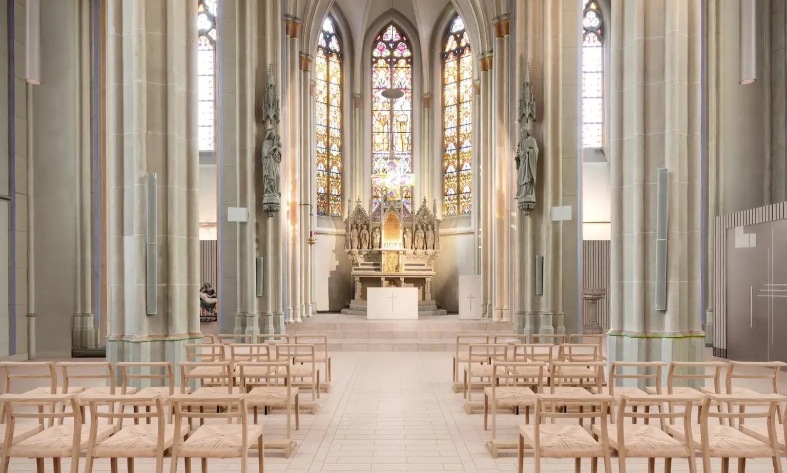 Innenansicht einer gotischen Kirche mit hohen Decken, bunten Glasfenstern und Holzbänken vor dem Altar