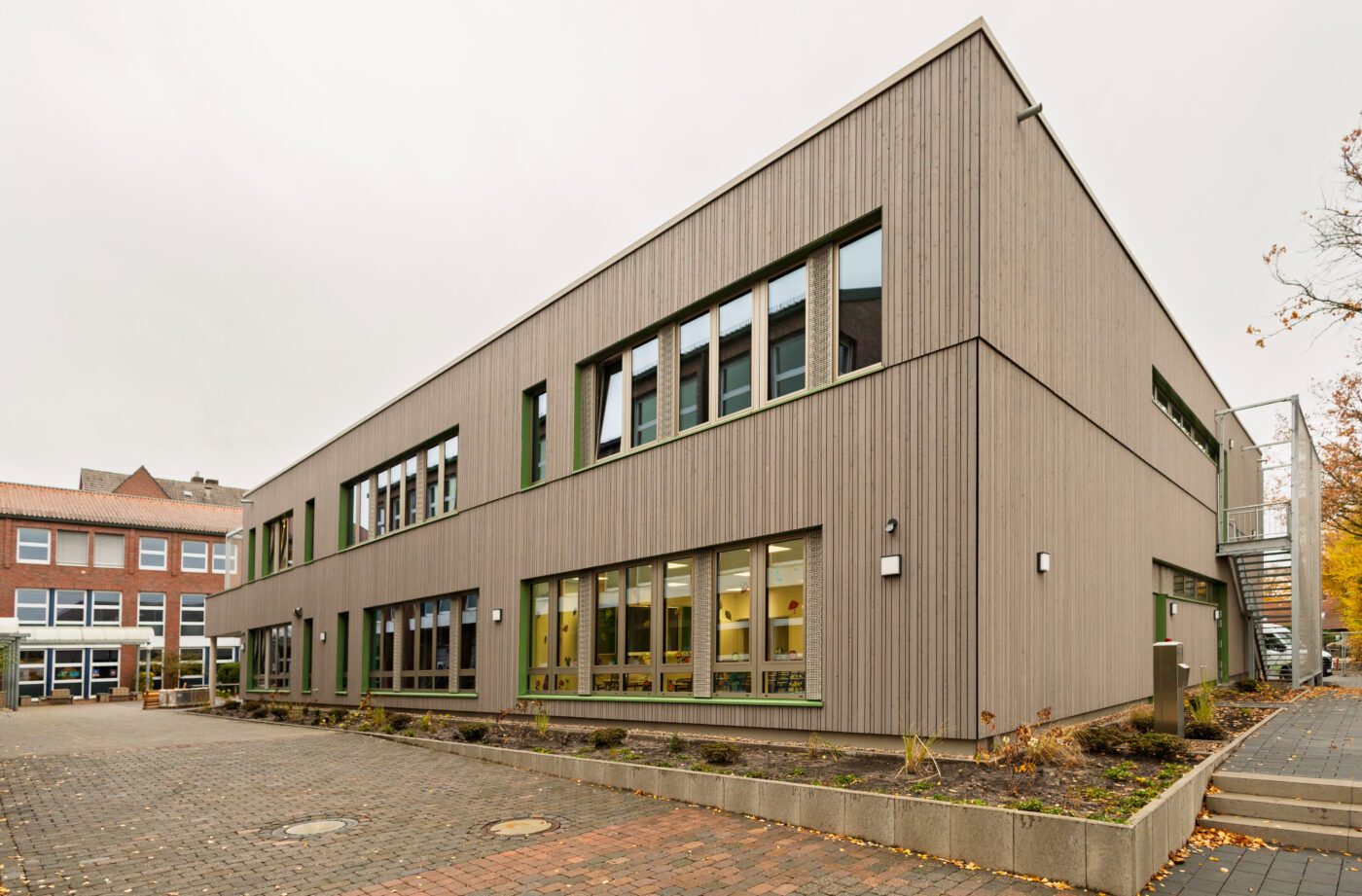 Modernes zweist&ouml;ckiges Geb&auml;ude mit Holzfassade und gro&szlig;en Fenstern, Herbstlandschaft im Hintergrund