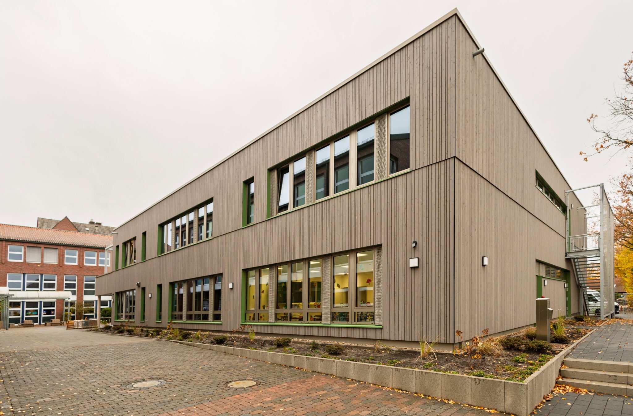 Modernes zweist&ouml;ckiges Geb&auml;ude mit Holzfassade und gro&szlig;en Fenstern, Herbstlandschaft im Hintergrund