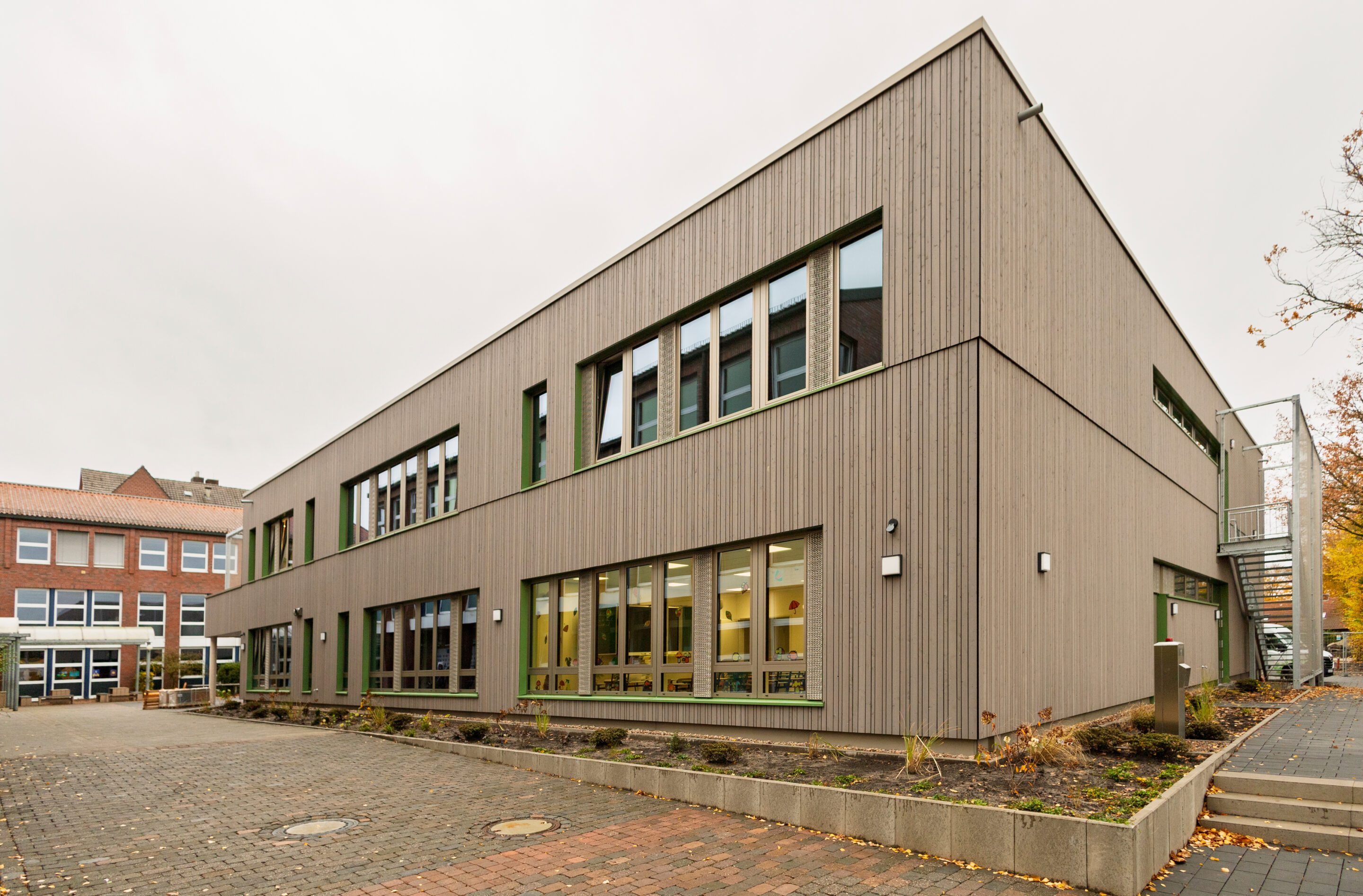 Modernes zweistöckiges Gebäude mit Holzfassade und großen Fenstern, Herbstlandschaft im Hintergrund